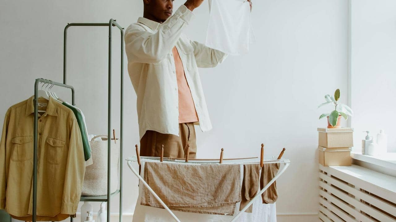 A man hanging clothes on a drying rack in a bright room.