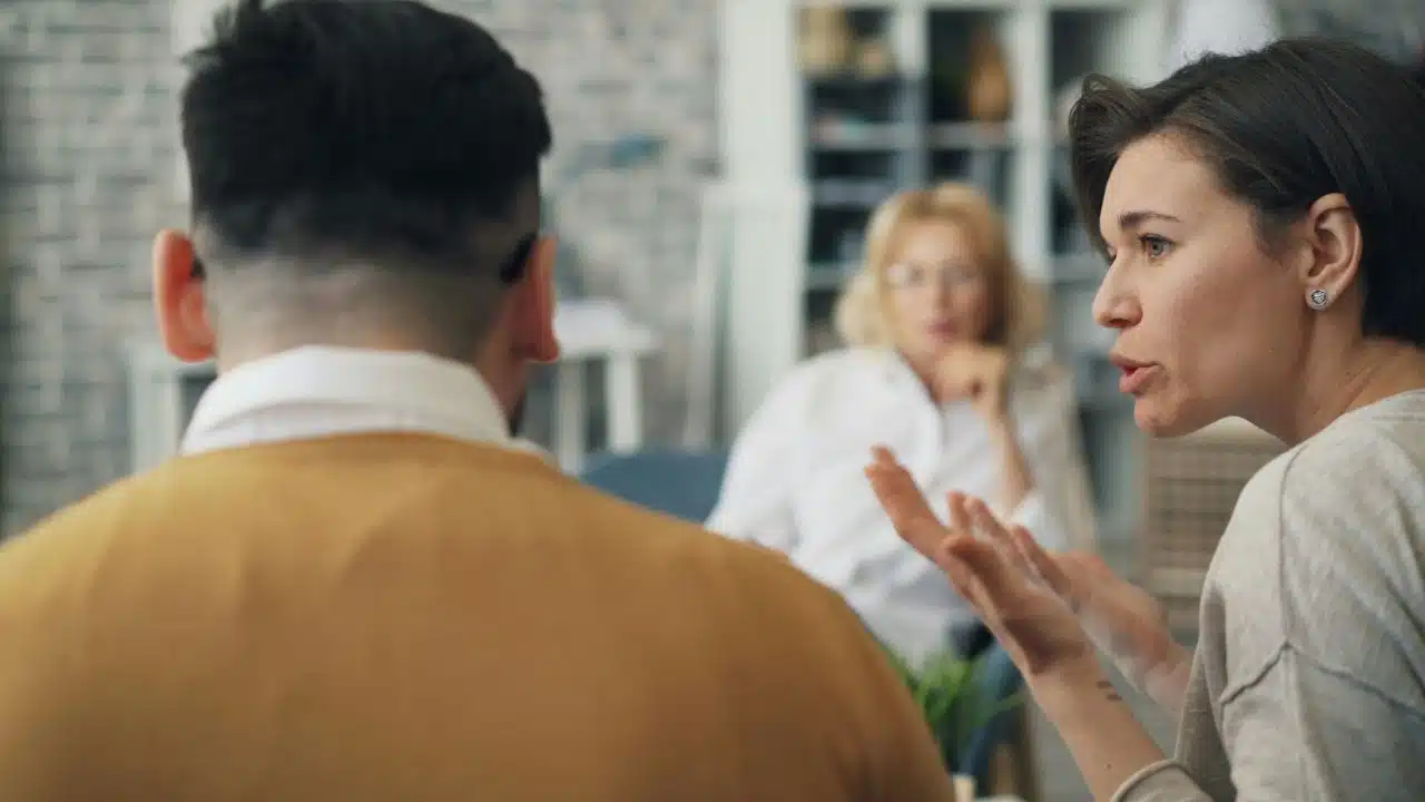 A woman gestures with her hands while talking to a man whose back is visible.