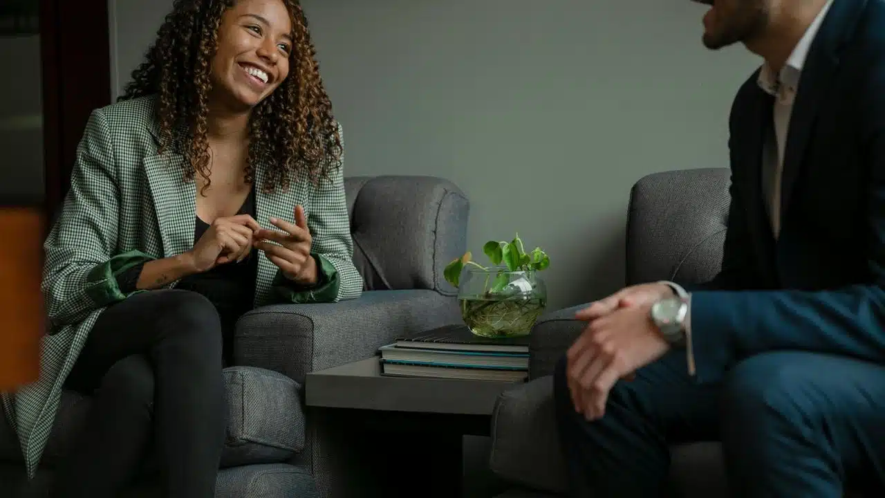A woman smiling and talking with a man while seated in a cozy indoor setting.