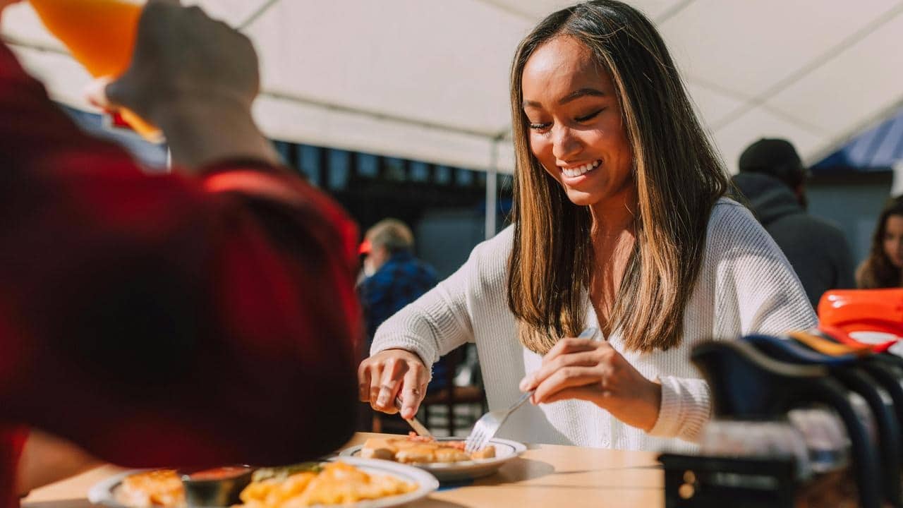 A woman smiling while eating a meal at an outdoor restaurant.
