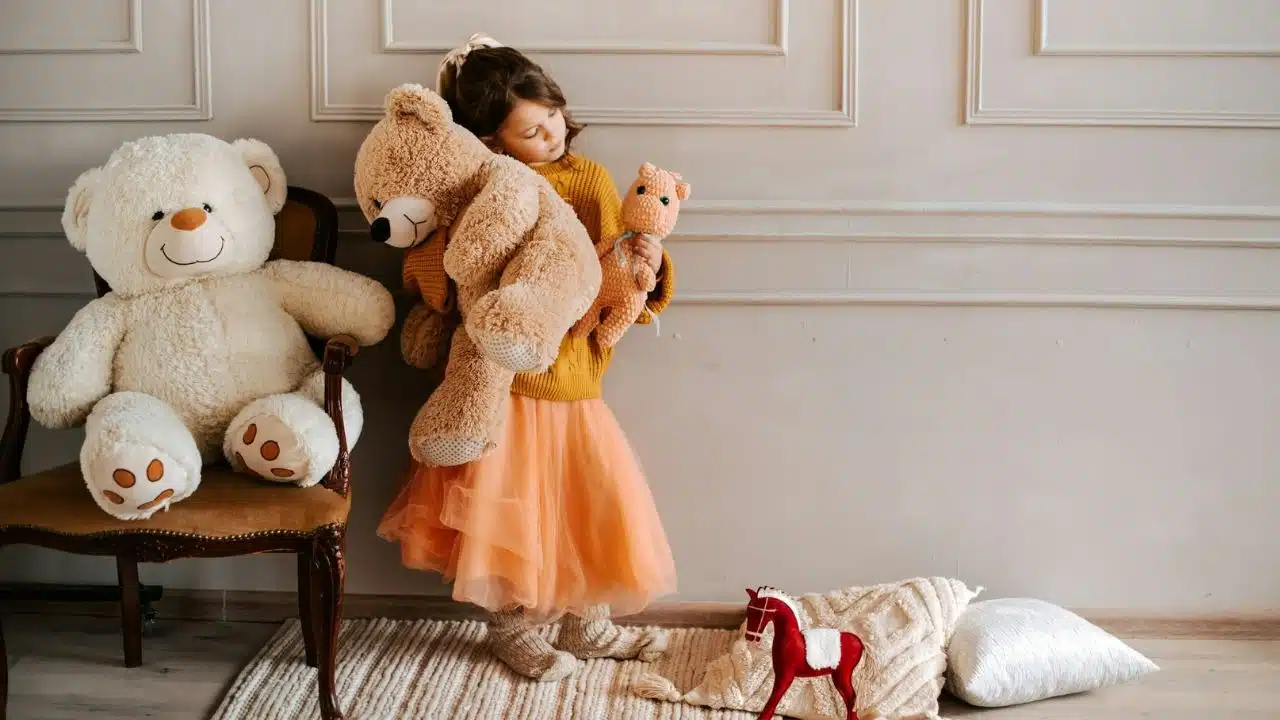 A young girl in a yellow sweater and orange skirt hugs a large teddy bear.
