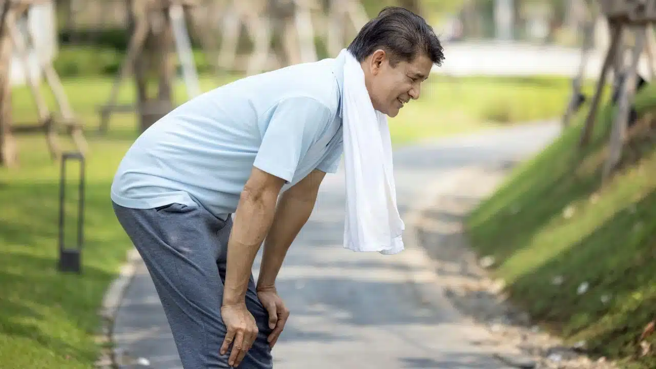 A man in athletic wear leans forward with hands on his knees on an outdoor path.