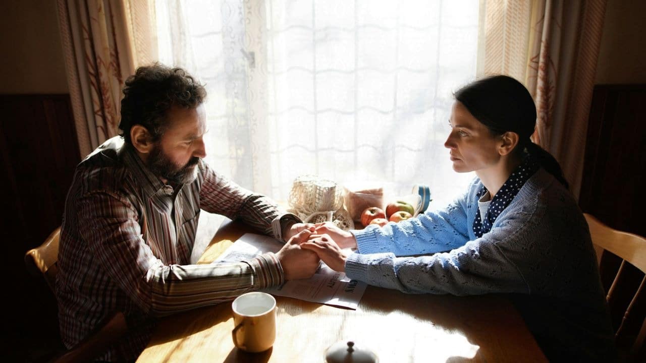 A man and woman sit at a table holding hands and looking at each other.