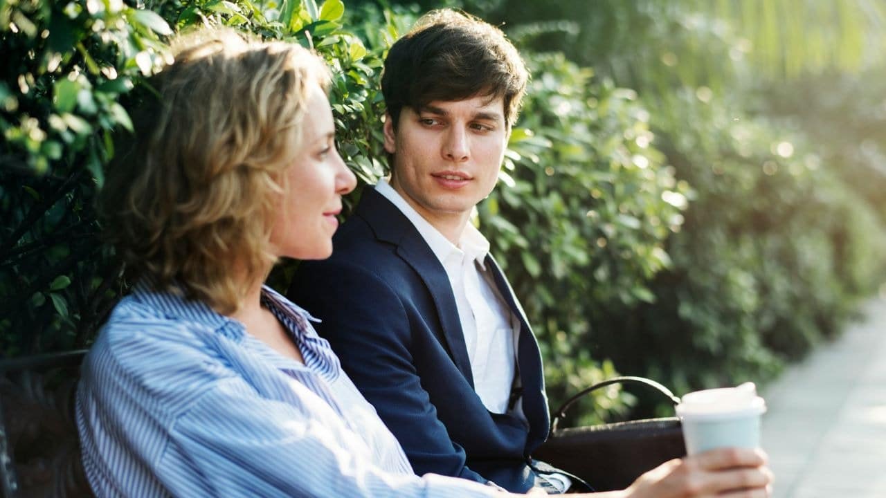 A man in a suit looks at a woman while sitting on a park bench outdoors.