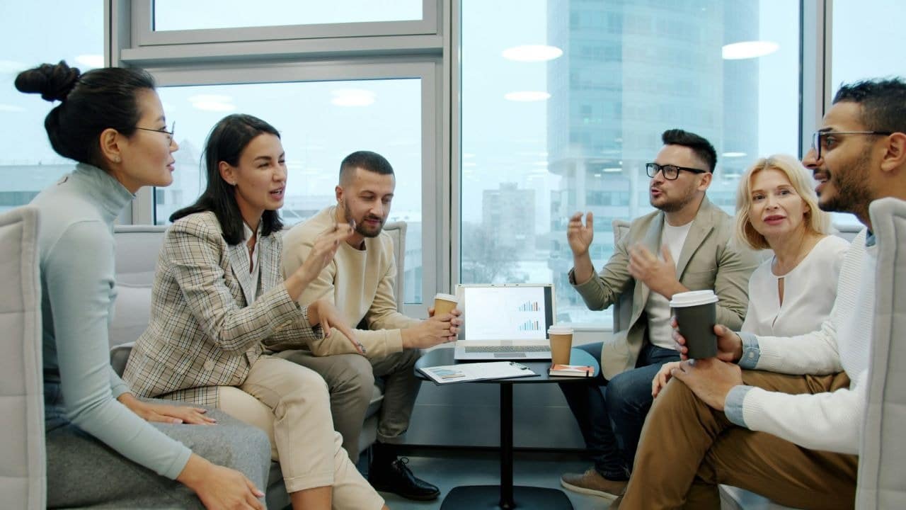 A diverse group of people sit in a circle having a discussion in a modern office.