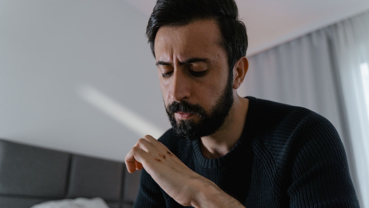 A bearded man looking at his nails.