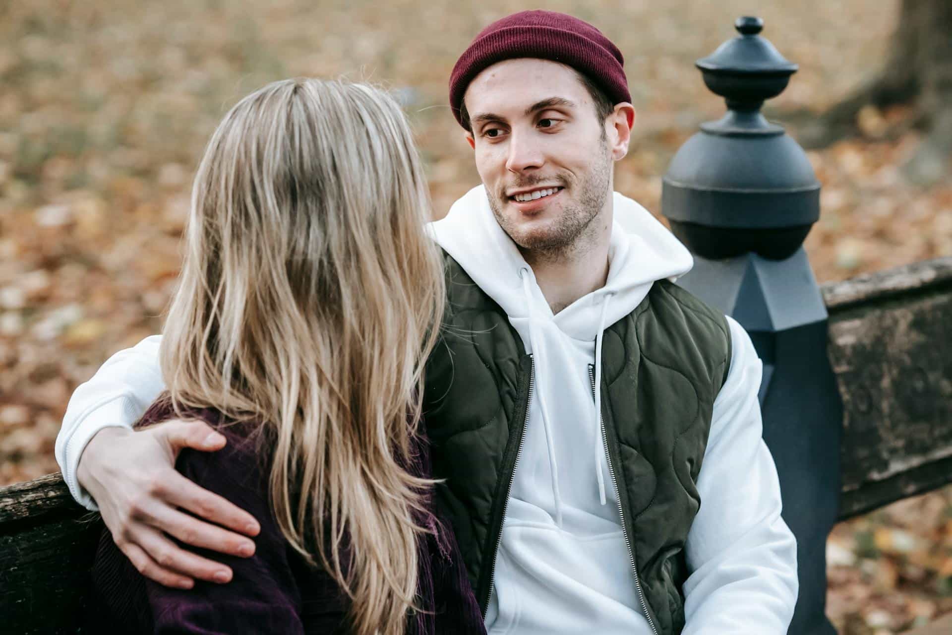 The man is looking lovingly at his woman while sitting on a park bench.