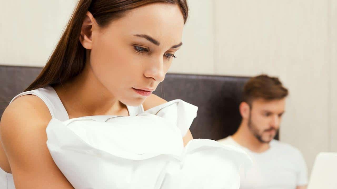 A woman is looking sad while a man works on his laptop in the background.