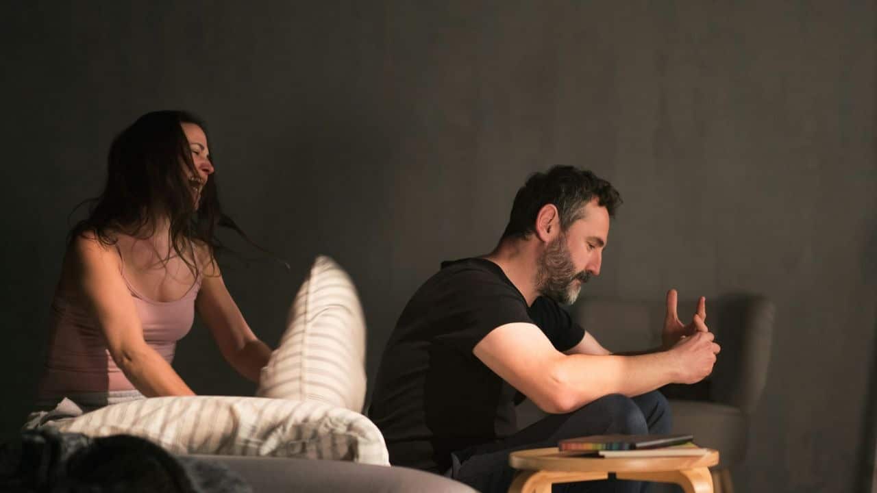 A woman yelling and throws a pillow at a man who sits facing away from her.