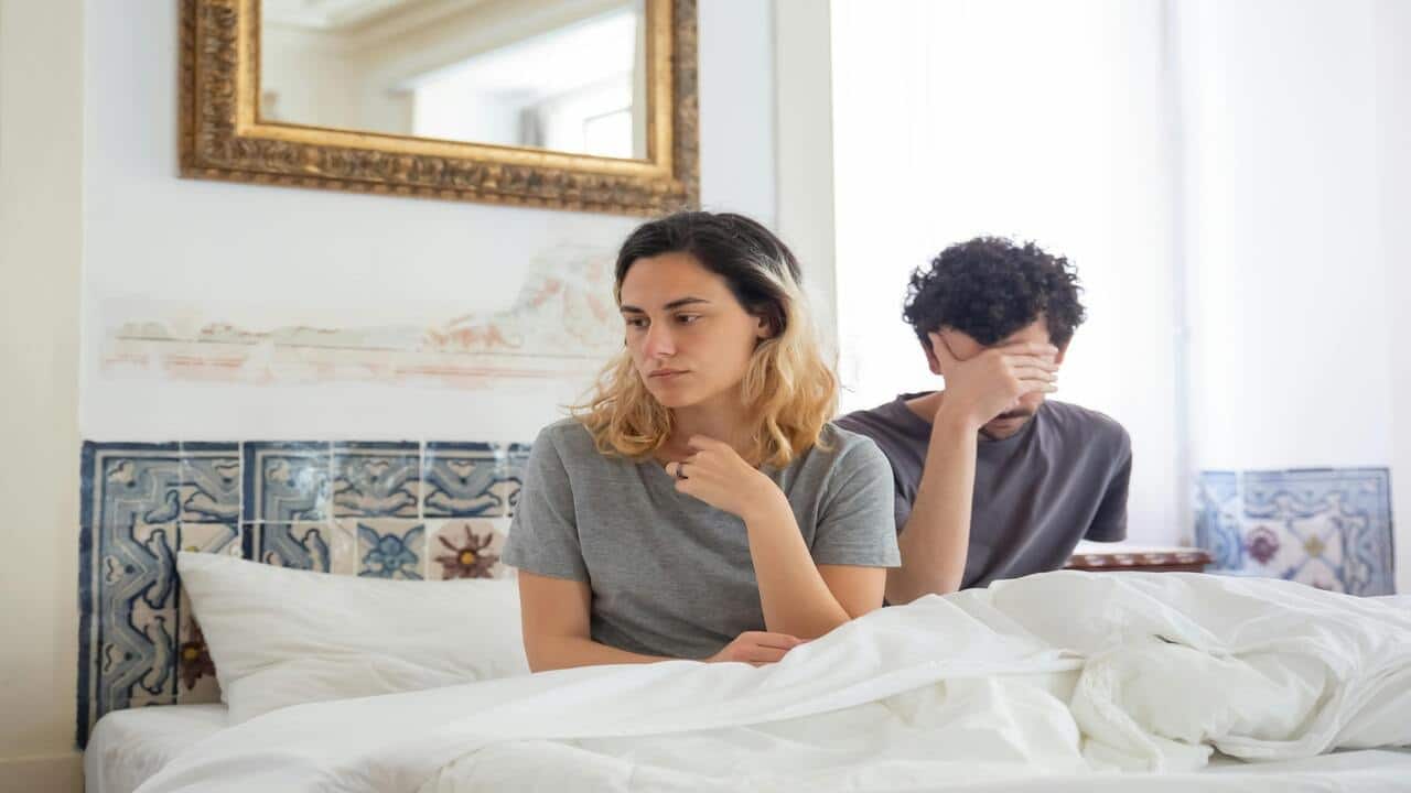 A woman and a man sitting on bed looking sad