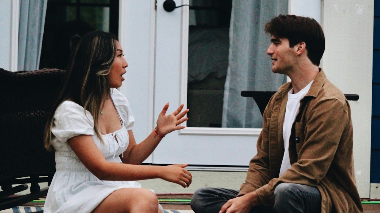 A woman talking to a man as they sit on the outside of a house.