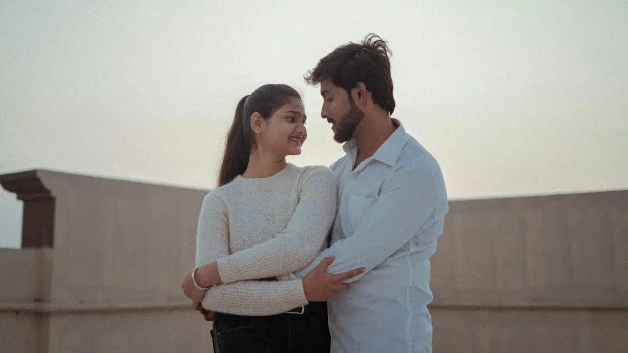 A couple hugging each other while standing on the rooftop of their home.