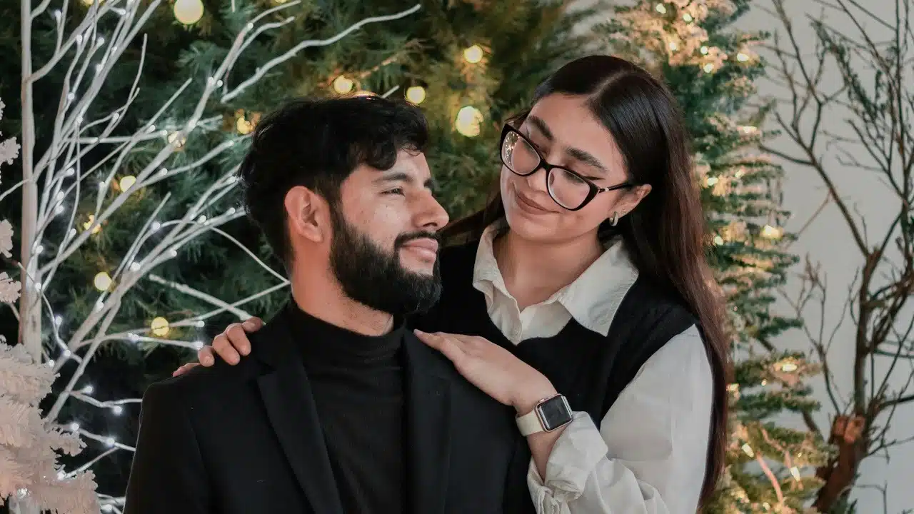 A couple posing for a picture in front of a Christmas tree.