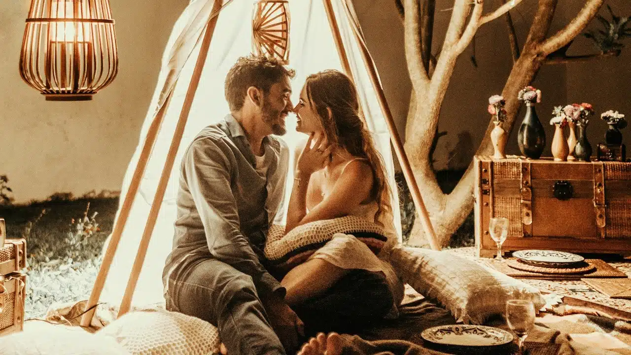 A couple sitting in a makeshift tent in their living room and sharing a tender moment.