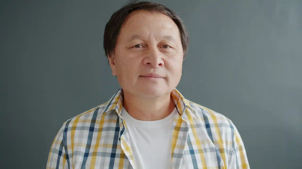 An older Asian man wearing a plaid shirt.