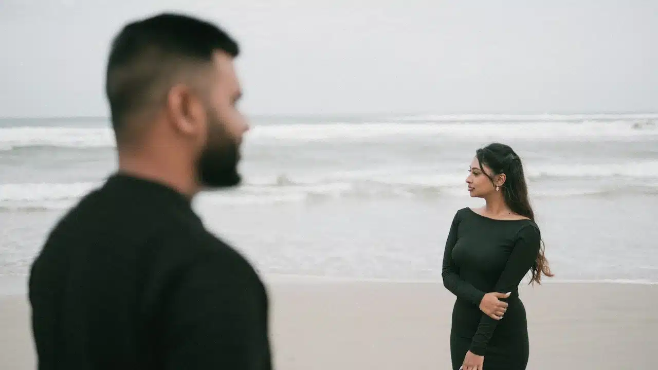 A couple on the beach are facing the ocean.