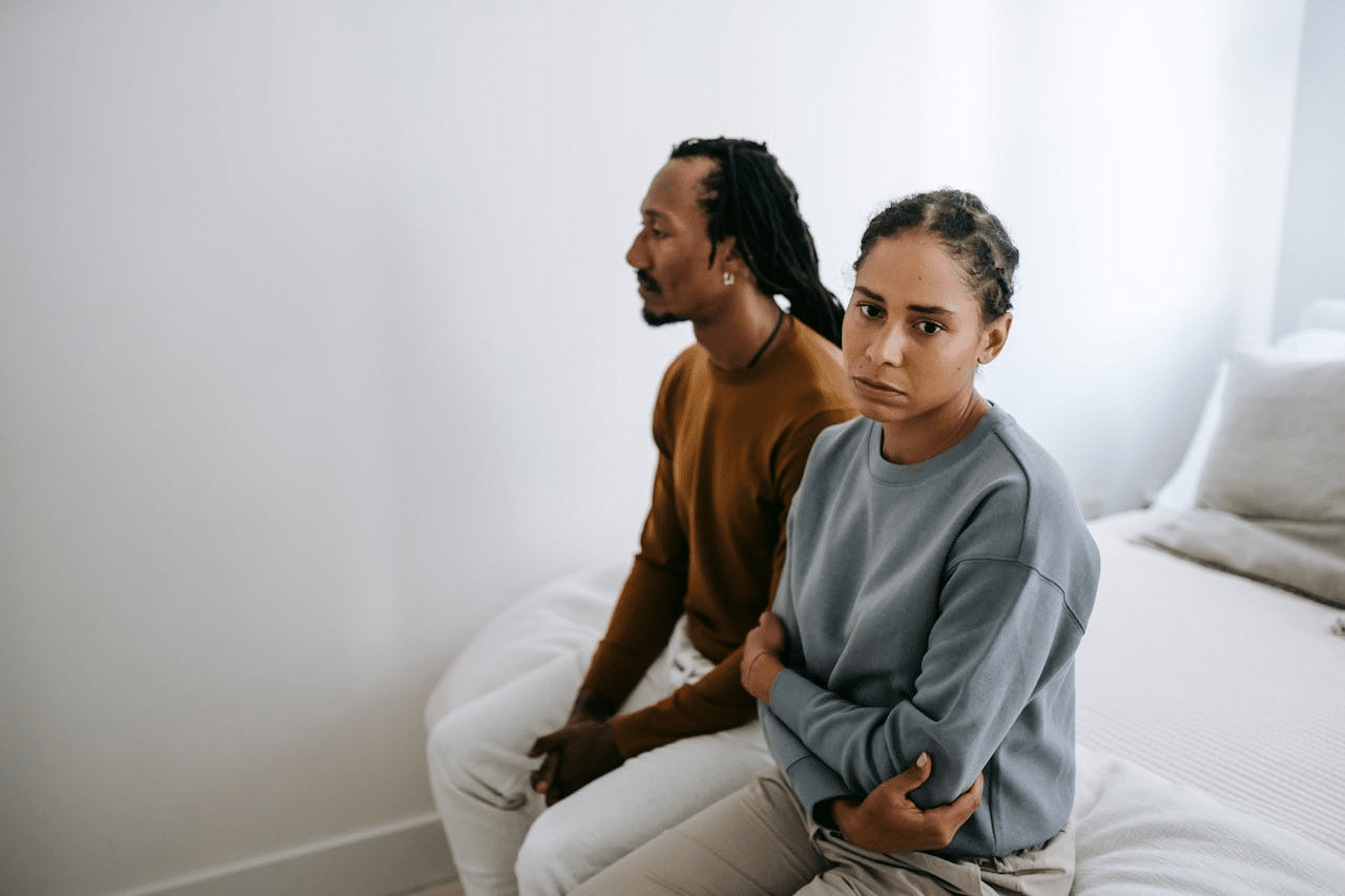 An unhappy Black couple sitting on a bed together.