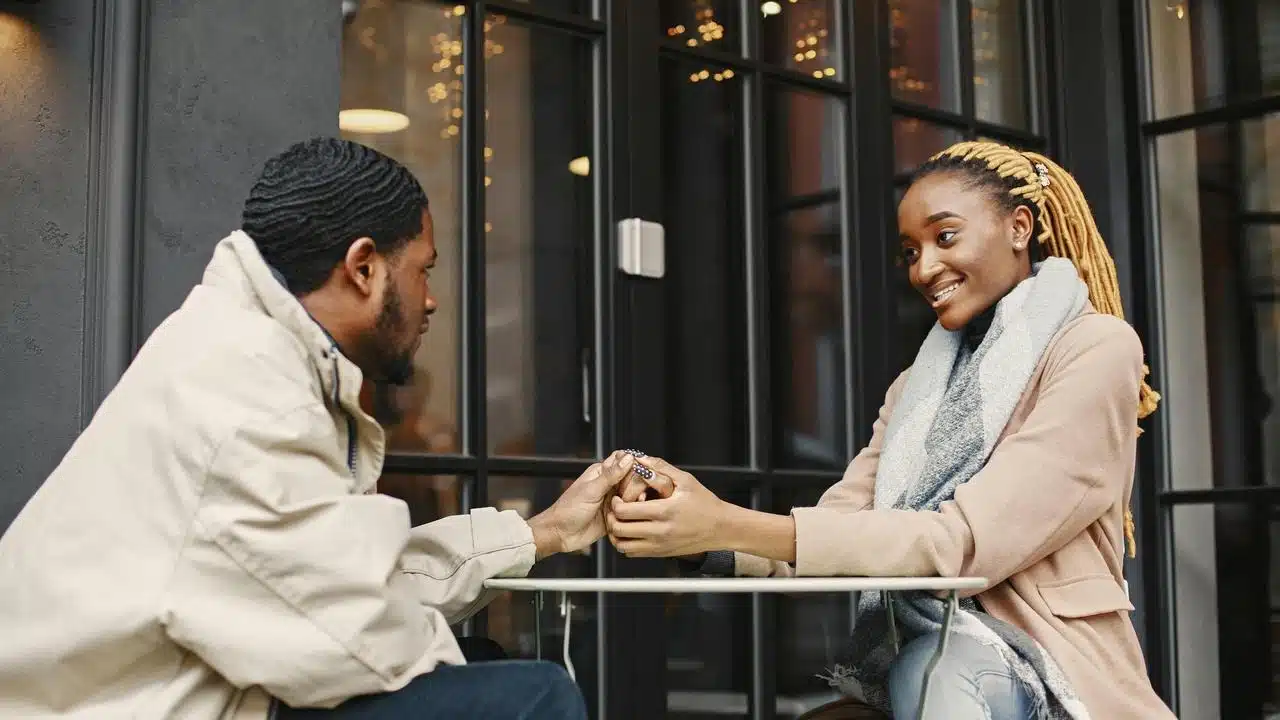 A man giving a ring to a smiling woman while sitting at an outdoor table.
