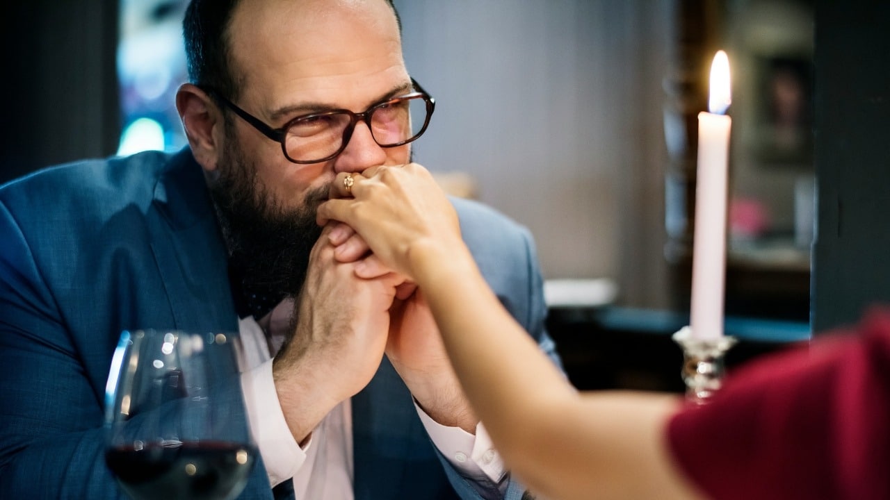 A man in a suit leans forward and kisses a woman's hand at a table.