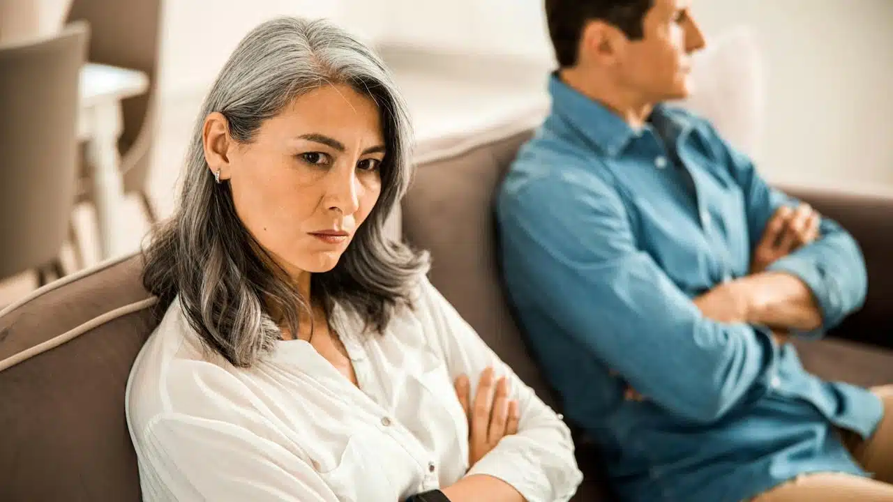 A mature couple is sitting on a couch and refusing to talk to each other.