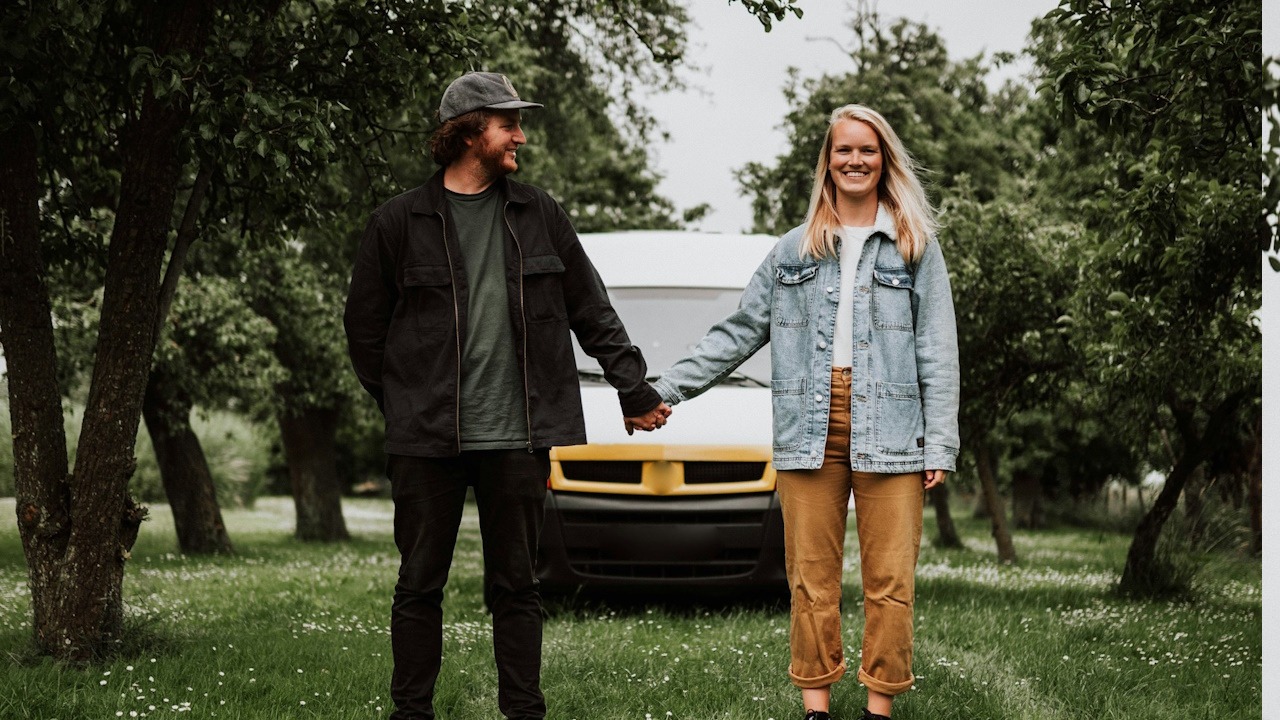 A couple holding hands while they are standing in a garden in front of a truck.