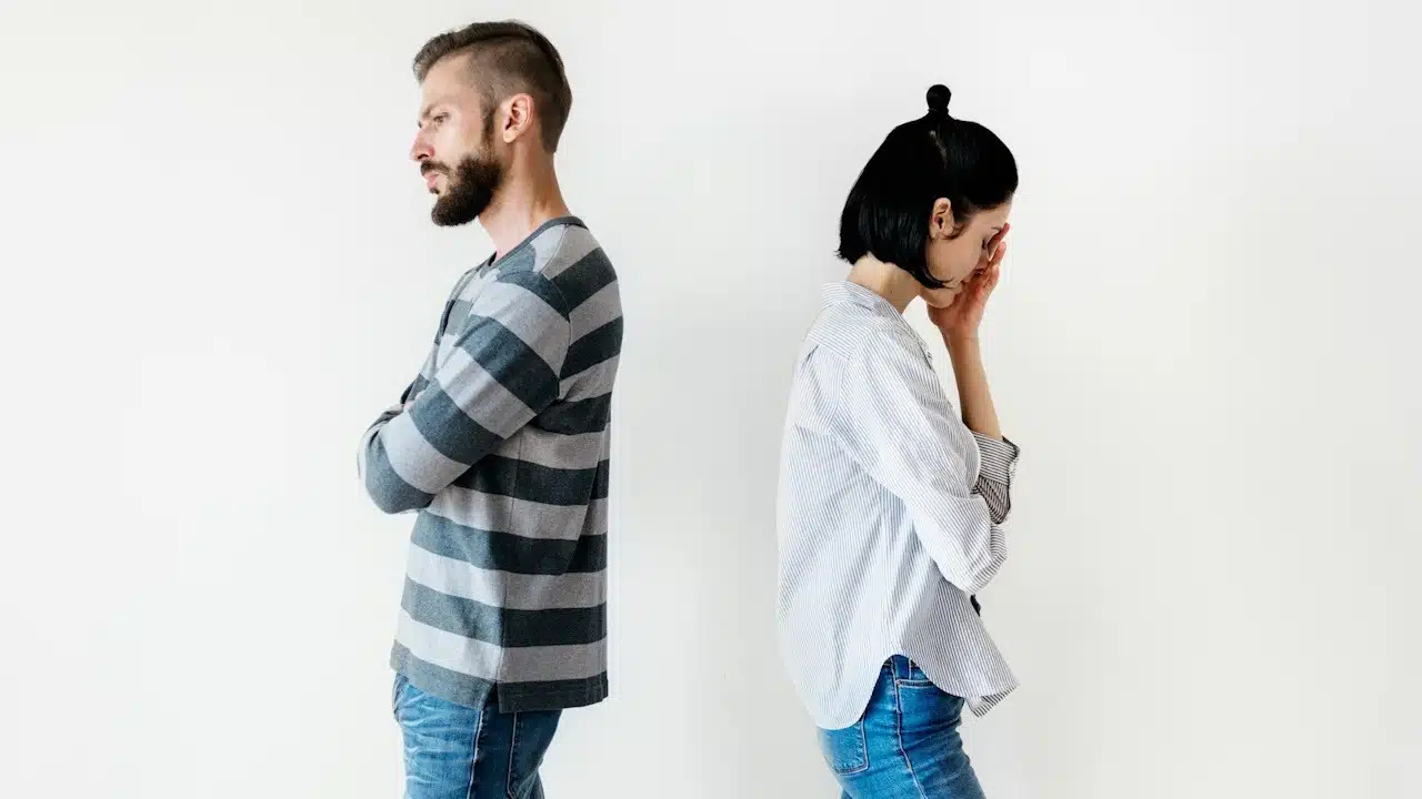 An upset couple standing with their backs against each other.