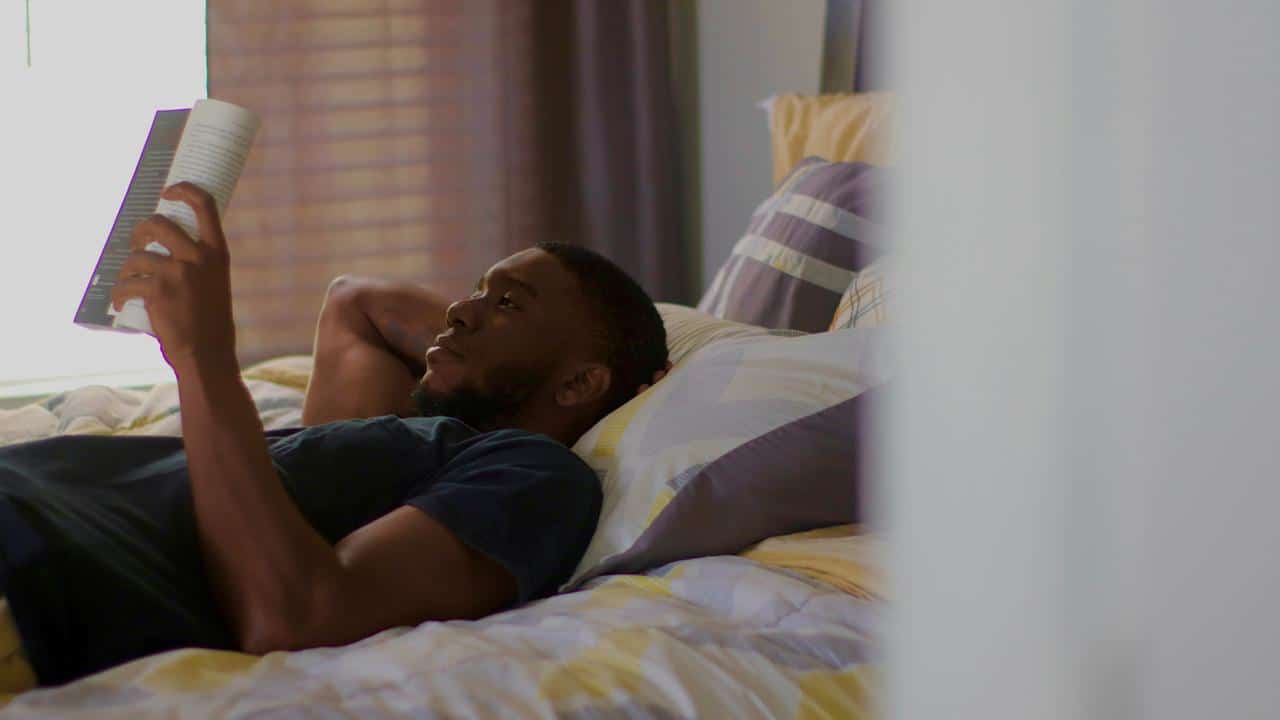 A man lying on a bed reading a book in a relaxed setting.