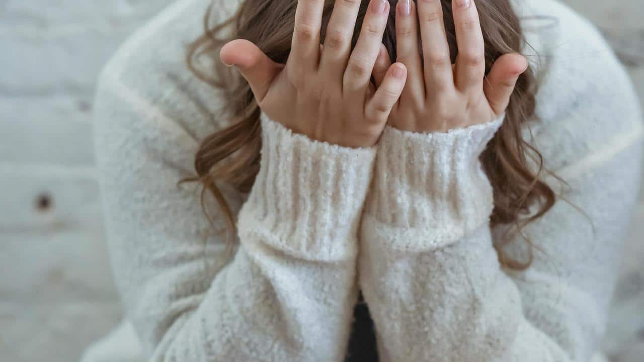 A person covering their face with their hands while sitting.