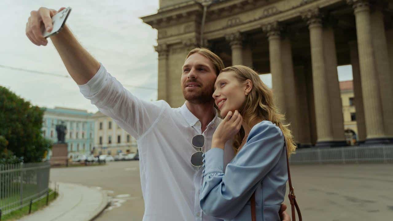 A couple taking a selfie in front of a large building.