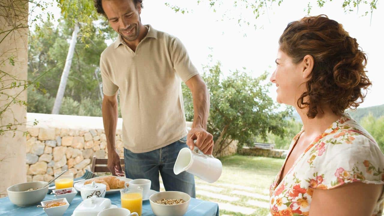 A man pouring coffee while sharing breakfast with a woman outdoors.