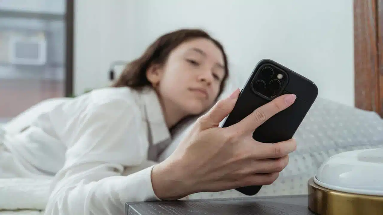 A woman lying in bed looking at her phone.