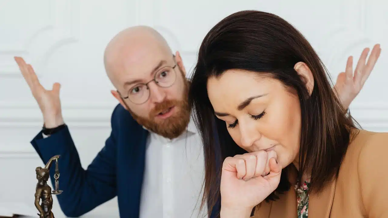 A man with glasses making fun of his partner who looks perturbed with closed eyes.
