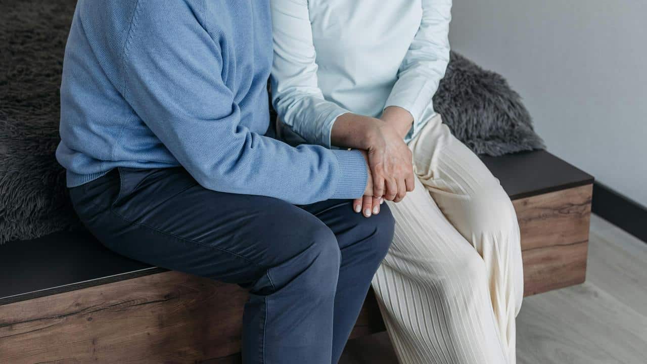 A couple sitting on a bed holding hands.