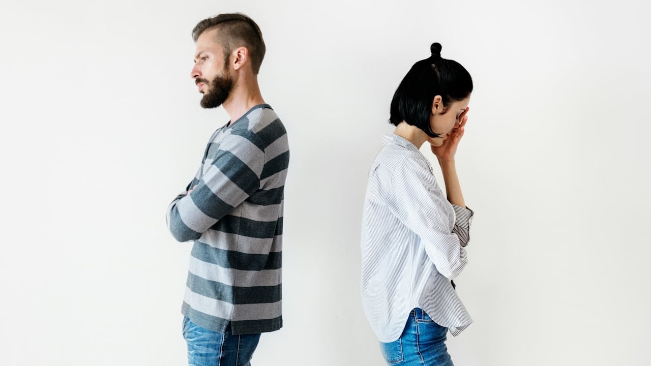 A man refusing to talk to a woman with his back to her while she looks sad.