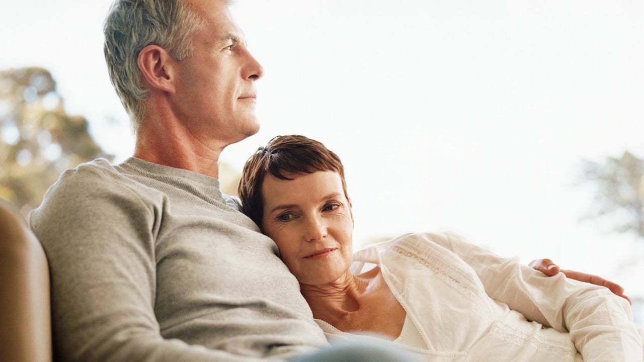 A middle-aged woman is resting her head on the shoulder of a man while they sit together.