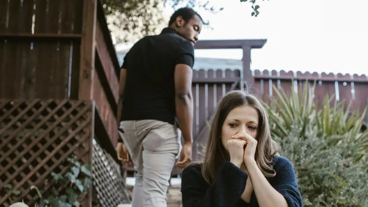 A woman sits outside with her hands to her face as a man walks away.
