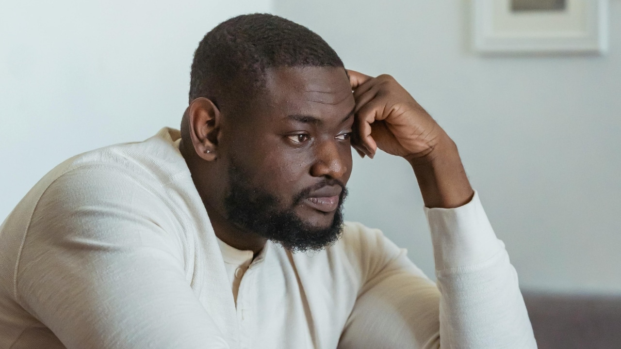 A man with a beard rests his head on his hand and looks sideways.
