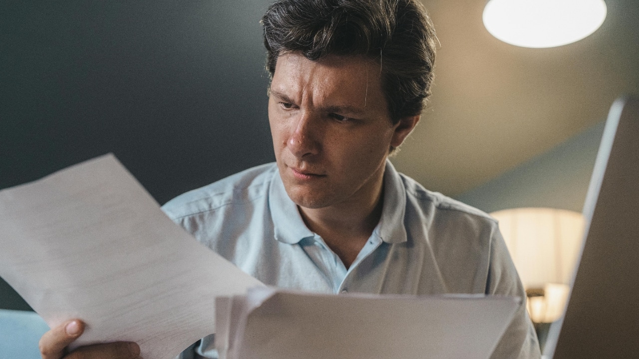 A man in a blue shirt holds and looks intently at a stack of papers.