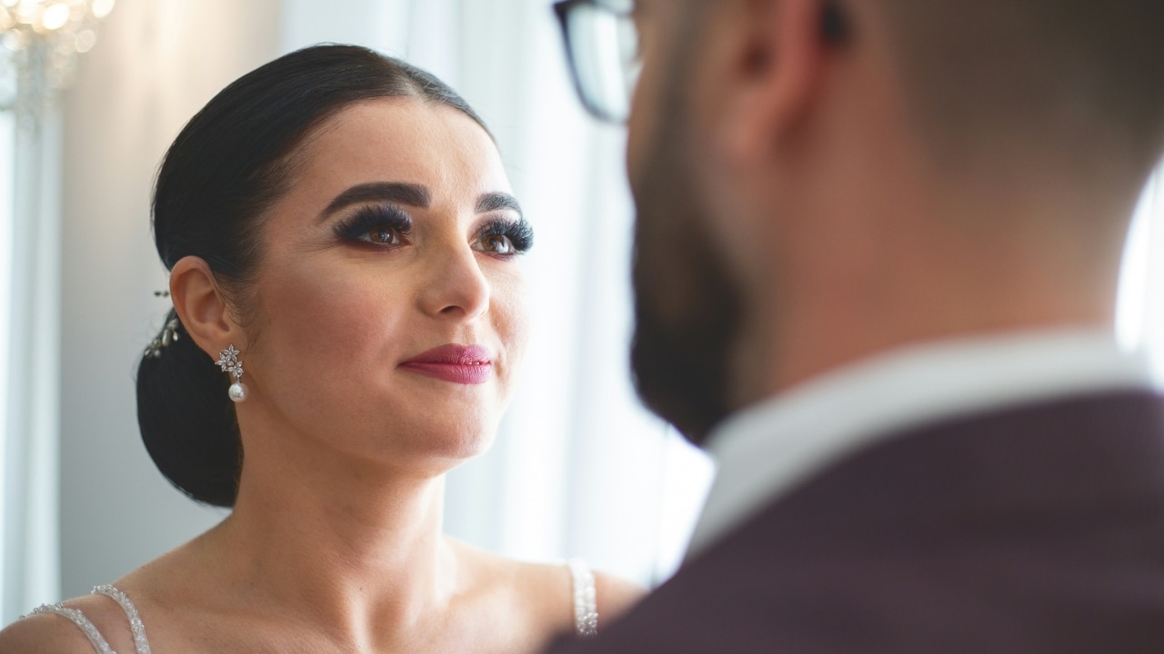 A woman with dark hair and pearl earrings looks up at a man in glasses.