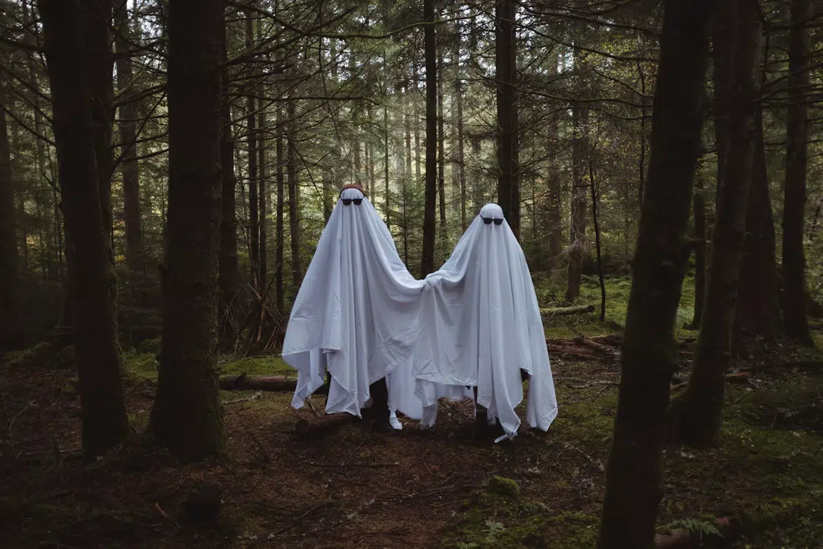 A couple dressed as ghosts in woods getting their picture taken.