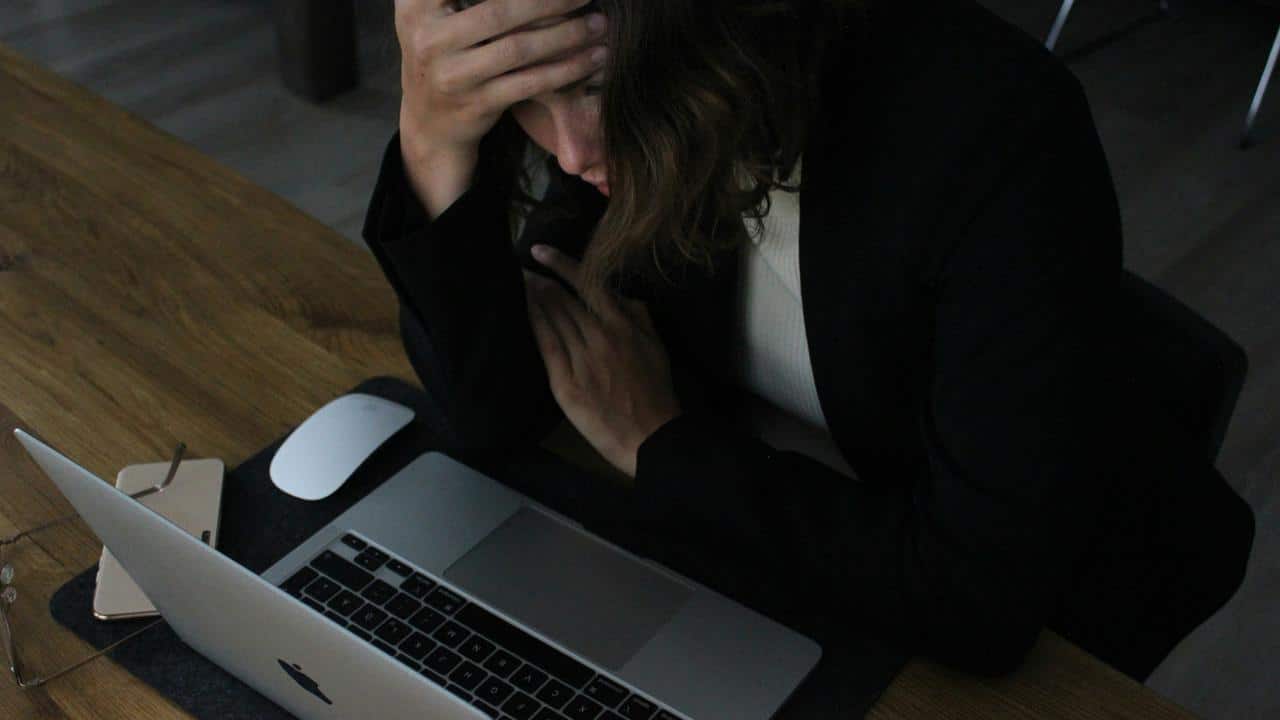 A person holding their head while looking stressed at a laptop on a desk.