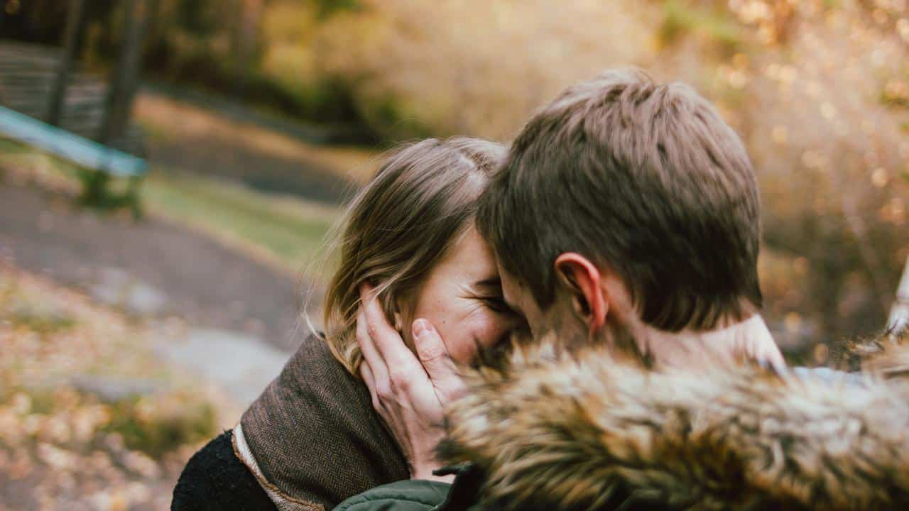 A couple shares a close moment outdoors in an autumn park.