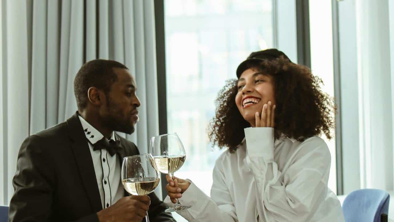 A dressed-up couple laughing and clinking glasses of white wine.