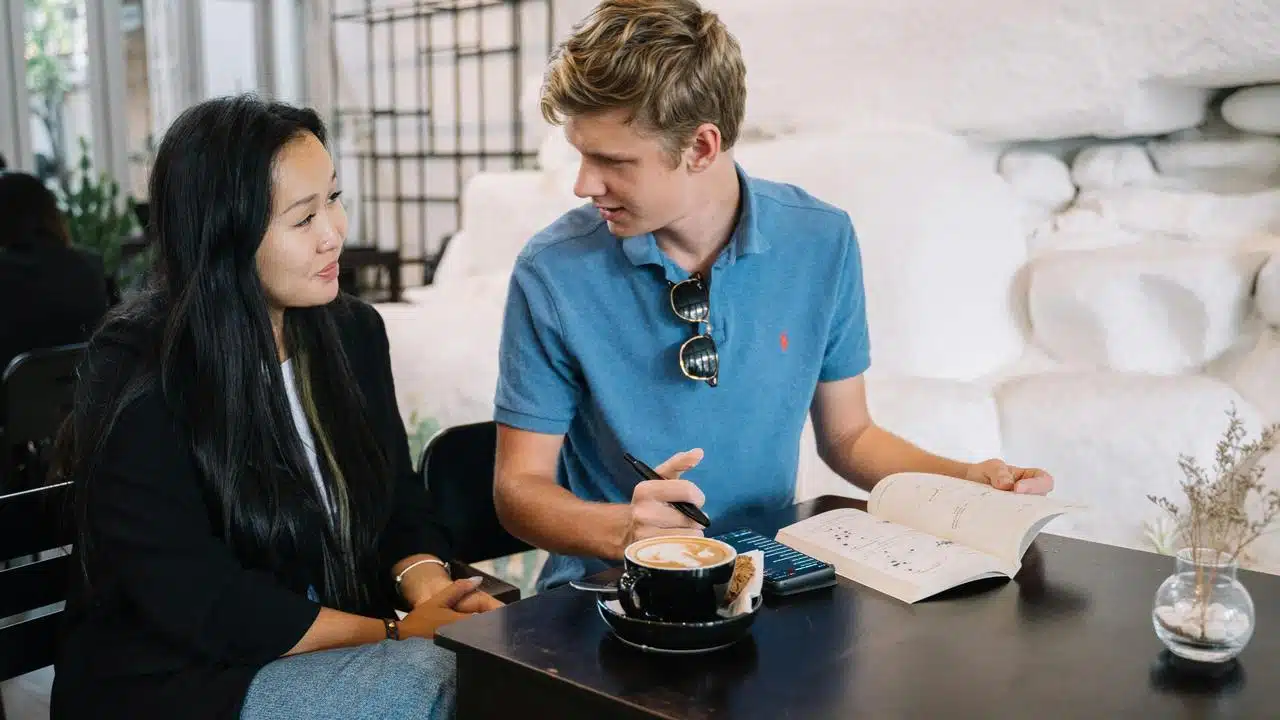 A man and woman discussing a book over coffee at a table.