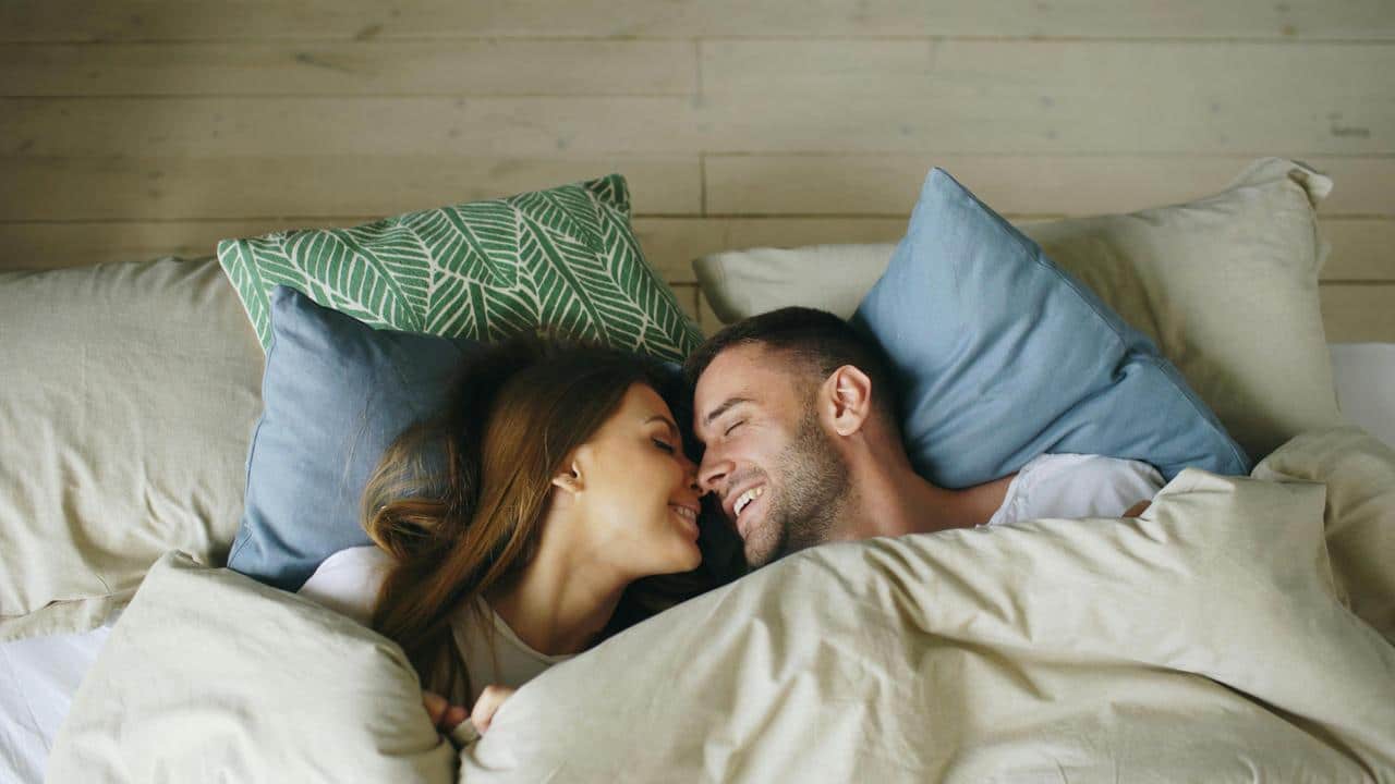 A couple lying in bed smiling at each other.