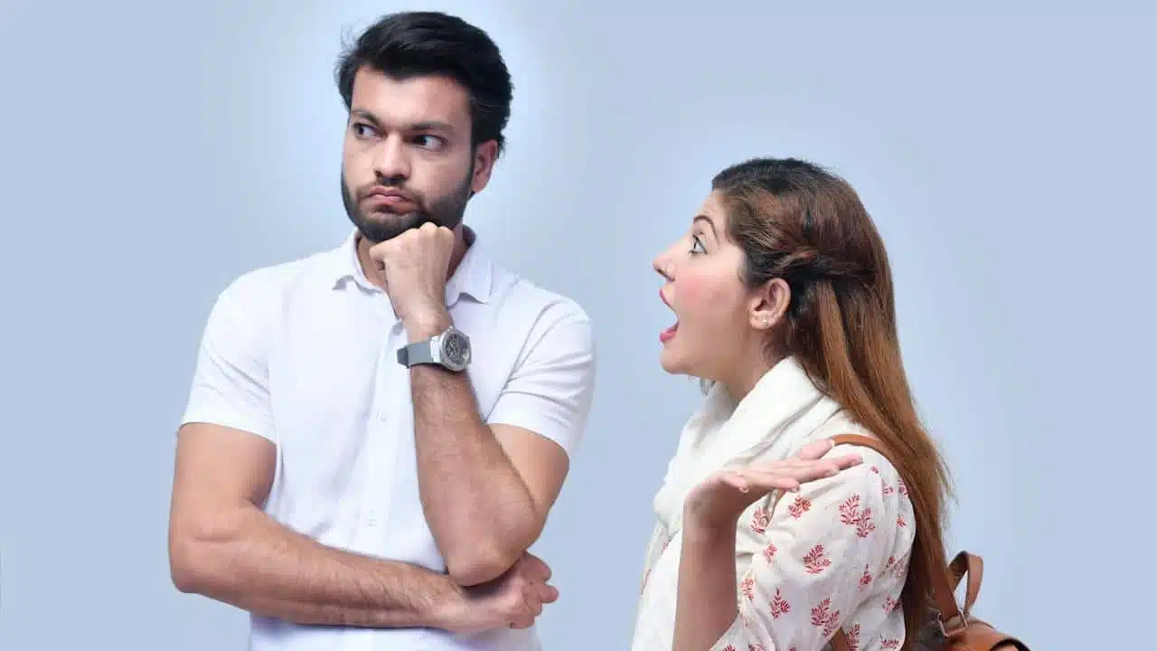 A woman shouting at a bearded man who looks to the side with a controlled expression.