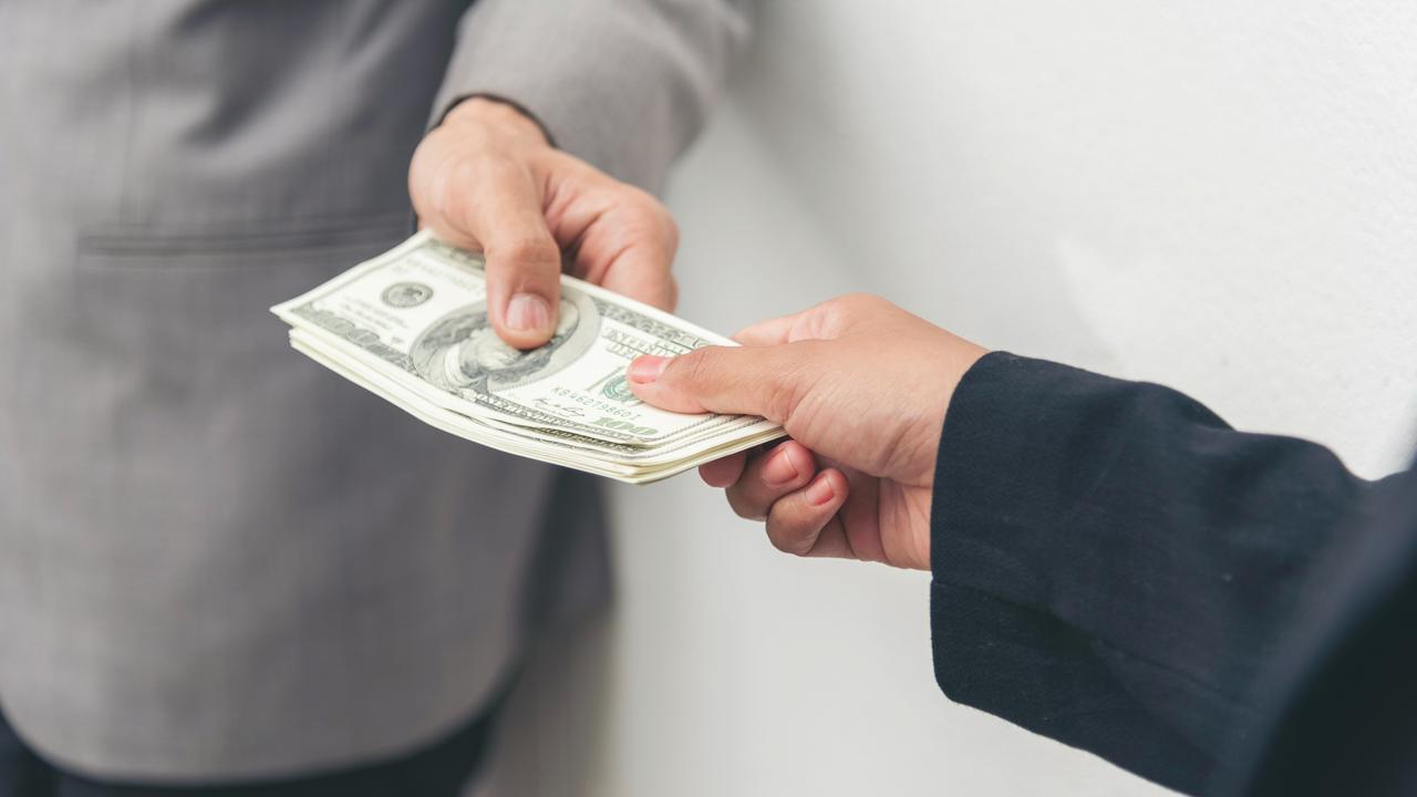 A stack of U.S. dollar bills being passed between two hands.