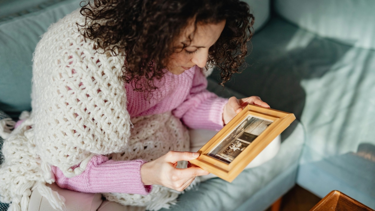 A woman with curly hair sits on a couch and looks at a framed photo.