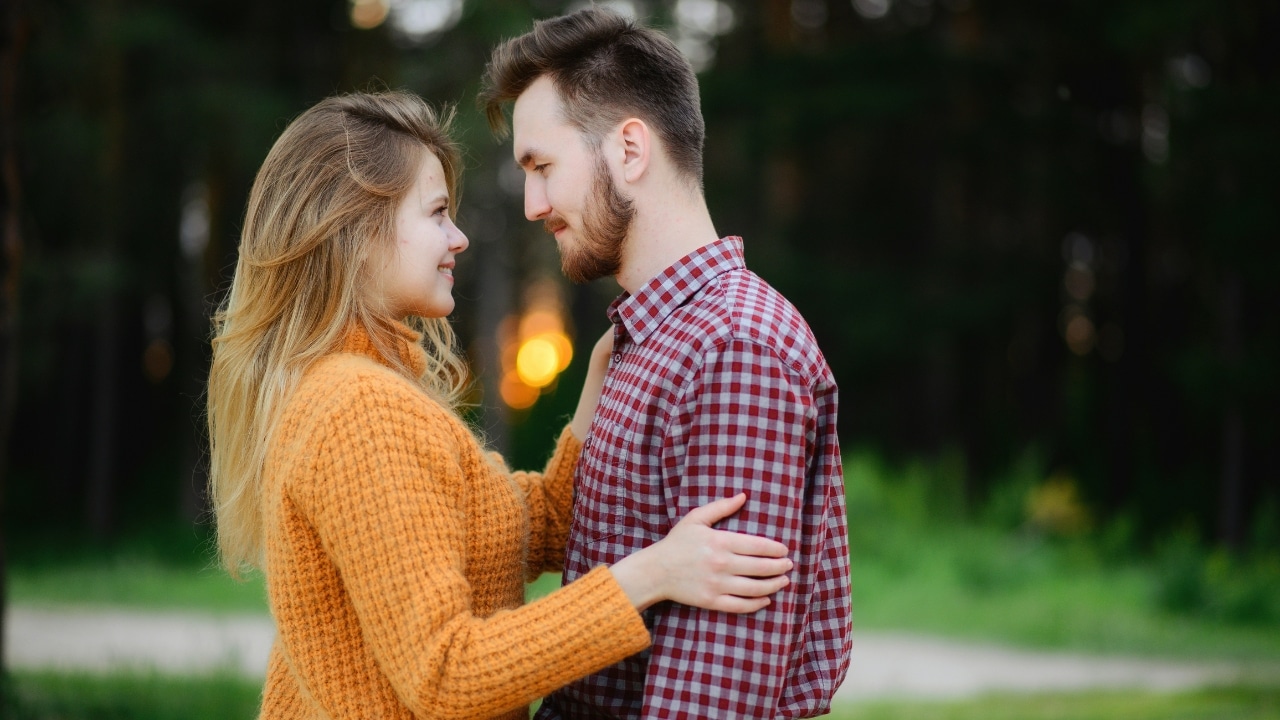 A man and woman in a park look into each other's eyes while holding each other.