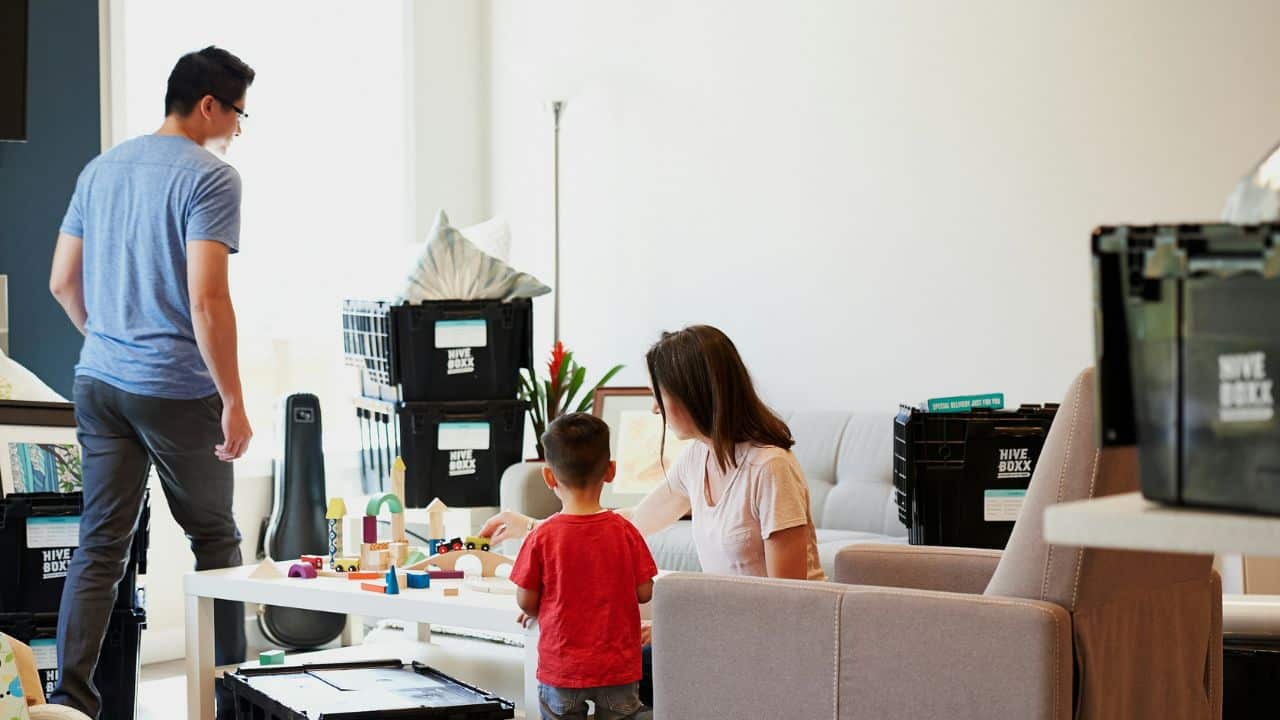 A woman and child play with blocks on a table while a man walks away.